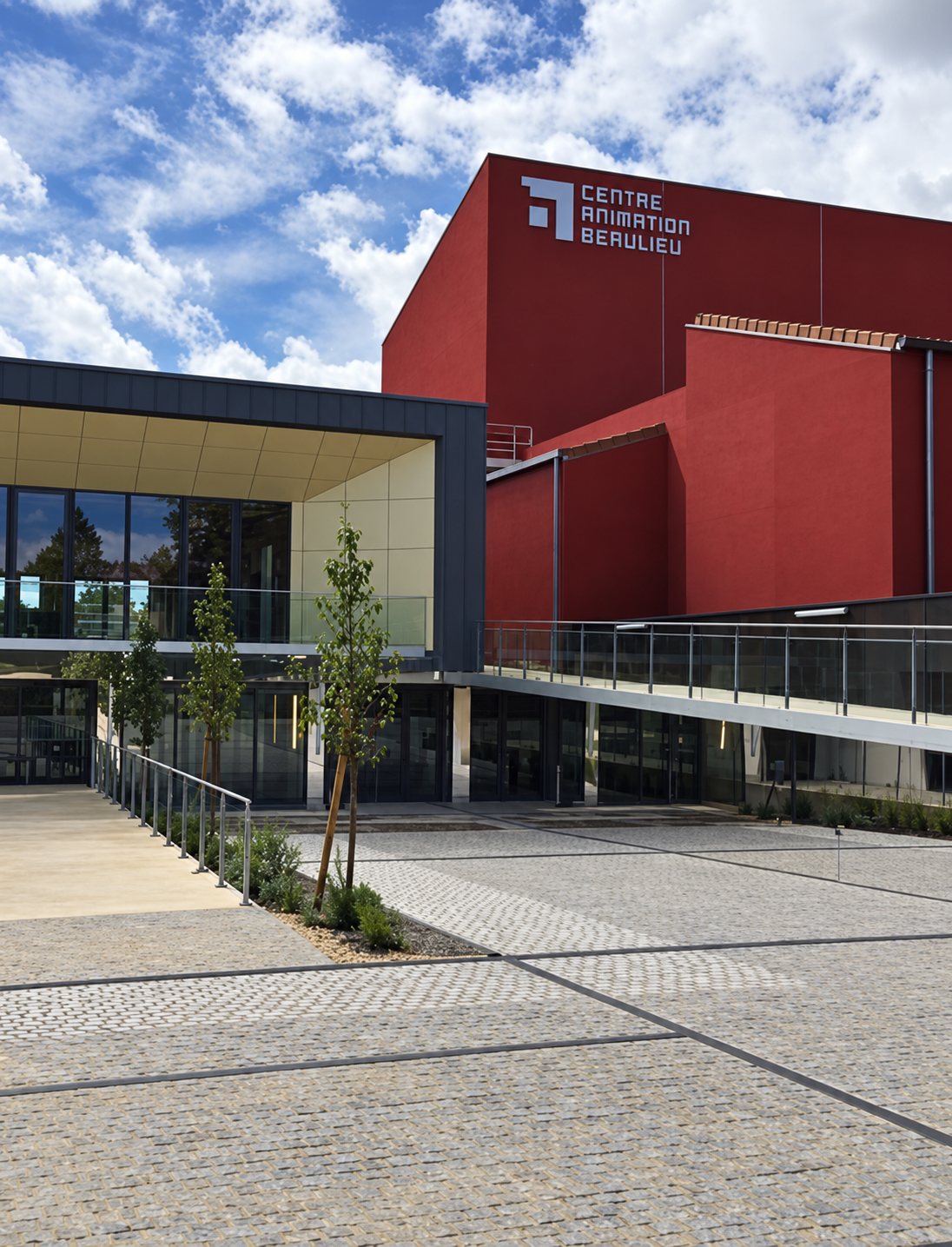 Bâtiment moderne rouge portant l'inscription Centre Animation Beaulieu, avec une entrée vitrée et un parvis pavé au premier plan.