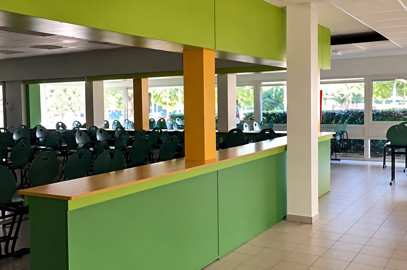 Intérieur d'une grande salle aux murs verts avec un comptoir en bois et de larges baies vitrées donnant sur l'extérieur.